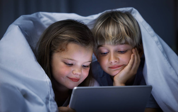 Shot of a brother and sister using a tablet in bed at night. - Фото, зображення
