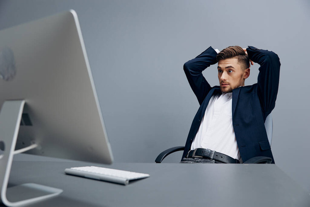 bel homme d'affaires assis à un bureau devant un fond gris ordinateur. Photo de haute qualité - Photo, image