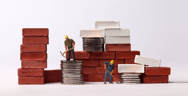 Miniature workers building bricks. Business concept with coins and miniature people. - 写真・画像