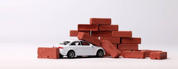 The concept of the dangers of car accidents. A miniature car that collided with a red brick. - Fotó, kép