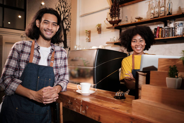 Two cafe business startup partners and friends, African American female, and Thai male baristas look at camera and cheerful smile at coffee shop counter bar as happy service job entrepreneurs. - Foto, Bild