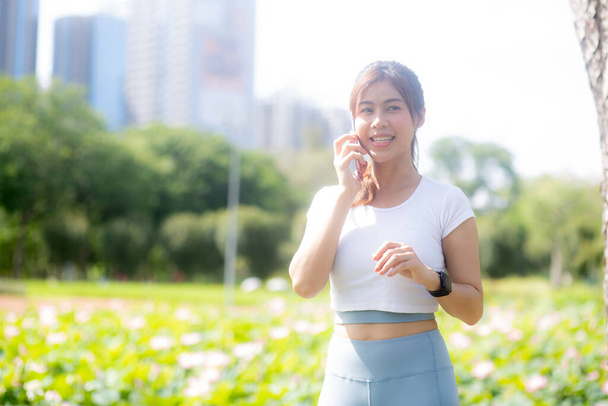 Happiness young asian woman standing and talking on smart phone in the park, girl relaxation and receiving smartphone and speaking on summer in the garden, lifestyles and communication concept. - 写真・画像