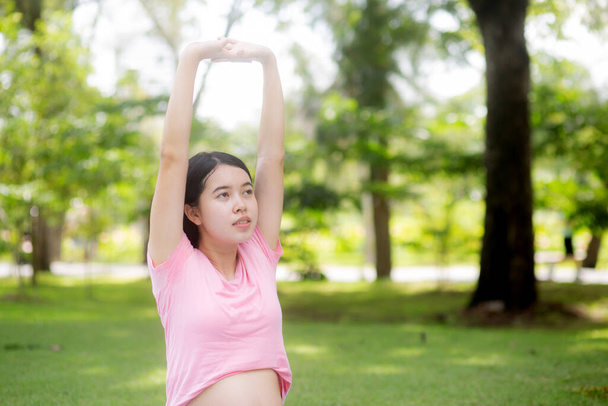 Happiness young asian woman pregnant sitting doing sport exercise with stretch hands muscle for health care at park, mother practicing yoga for leisure in the garden, activity for pregnancy concept. - Photo, image