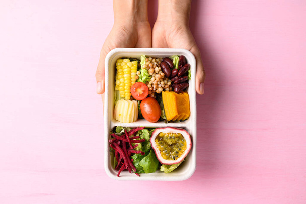 Friss zöldségsaláta biológiailag lebomló tálban, rózsaszín alapon kézzel, egészséges vegán étel - Fotó, kép