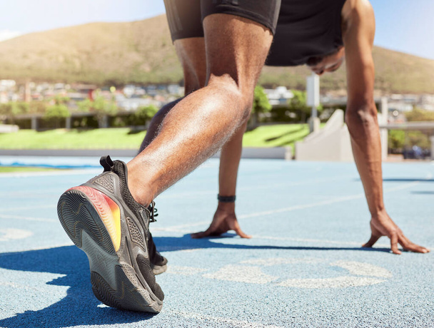 Close up of an athlete getting ready to run track and field with his feet on starting blocks ready to start sprinting. Close up of a man in starting position for running a race on a sports track. - Фото, зображення