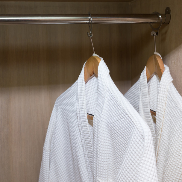 roupões de banho brancos pendurados no armário de madeira
 - Foto, Imagem