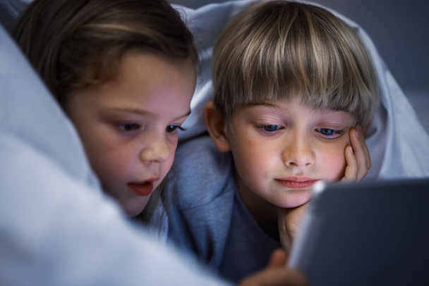 Shot of a brother and sister using a tablet in bed at night. - 写真・画像