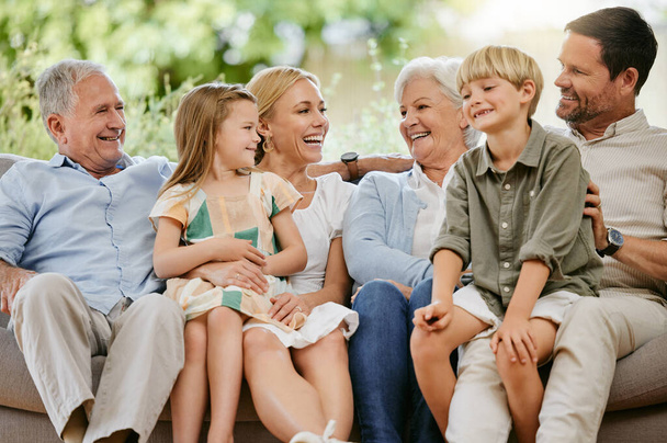 Счастливая и улыбающаяся многонациональная кавказская семья, сидящая рядом на диване дома. Счастливые обожаемые дети на выходных общаются с мамой, папой, дедушкой и бабушкой. - Фото, изображение
