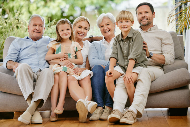 Portrait of a smiling multi generation caucasian family sitting close together on the sofa at home. Happy adorable children bonding with their mother, father, grandfather and grandmother on a weekend. - Valokuva, kuva