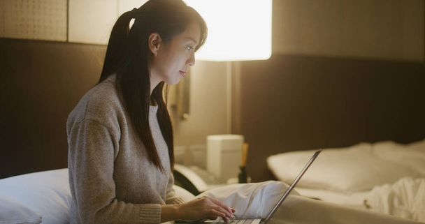 Жінка використовує ноутбук для роботи і сидить на ліжку вночі
 - Фото, зображення