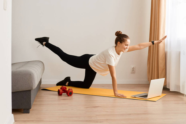 Cheerful active woman doing fitness at home, using laptop, watching online lessons, well-fit female in sportswear exercising watching fitness videos on Internet. - Photo, image