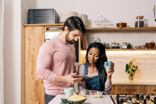Happy couple having breakfast in the kitchen at home and using tablet. - Photo, image