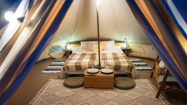 Tent interior with lamps, bed and furniture at glamping, night - Foto, Imagen