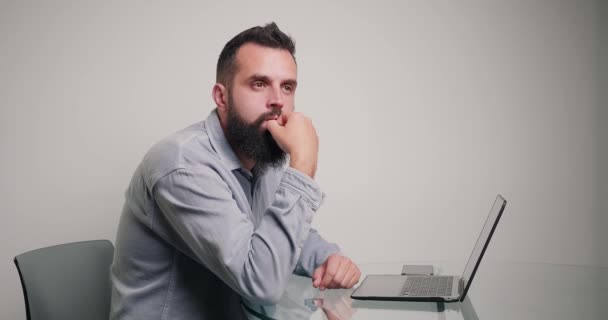 Skilled programmer writes code for website on laptop. Idea struck bearded freelancer sitting at desk in room against beige wall making money at home - Footage, Video