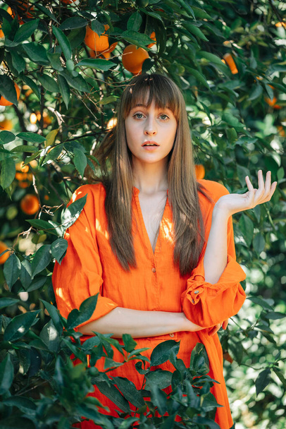 Pretty girl in orange dress is looking at camera in orange garden  - Zdjęcie, obraz