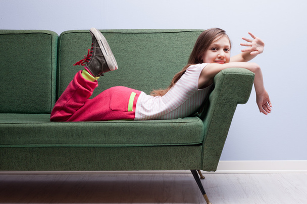 緑のソファーに横になっているカメラで手を振る少女 - 写真・画像