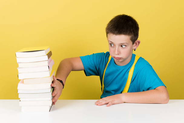 Cute schoolboy rejecting to study isolated on yellow background. Student boy moving away pile of books. - Foto, Imagem