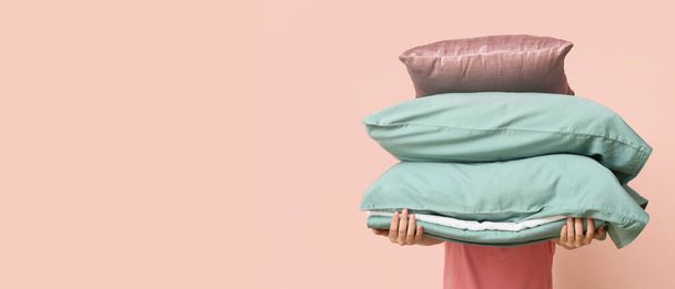 Woman holding soft pillows and bedsheets on pink background with space for text - Photo, Image