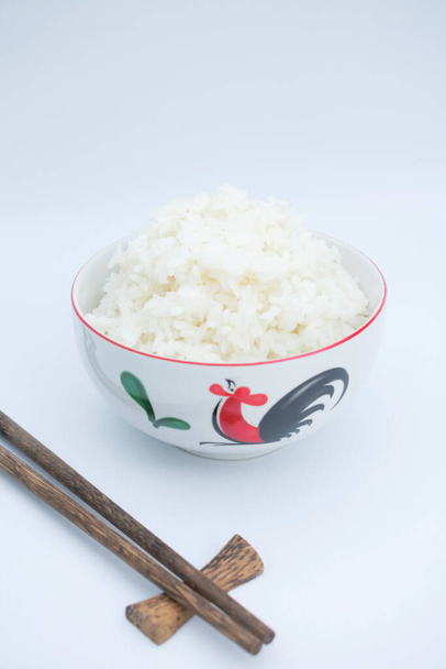 arroz en un tazón de cerámica con palillo de madera sobre fondo blanco - Foto, Imagen
