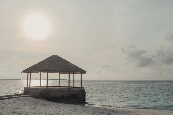 Ξημέρωμα στον ωκεανό. Μαλδίβες, η έρημη παραλία με το water cafe. Καλοκαιρινές διακοπές σε τροπικό νησί. Πολυτελή ταξίδια. Ηρεμία και χαλάρωση. Όμορφη θέα στη θάλασσα σε απαλά χρώματα. - Φωτογραφία, εικόνα