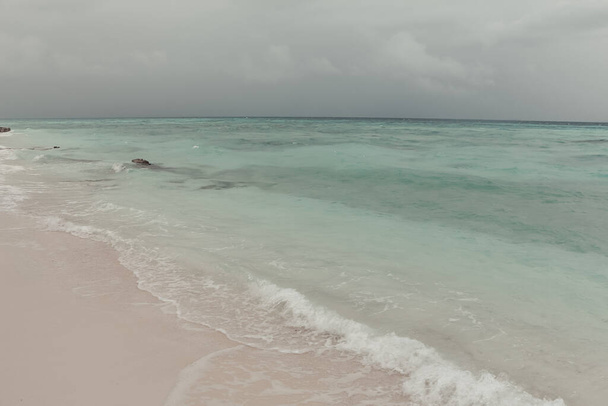 Sky with storm clouds over a calm sea. Maldives, a beach with the white sand near the turquoise ocean. Summer vacation on a tropical island. Luxury travel. Beautiful sea view in calm muted colors. - Foto, Imagem