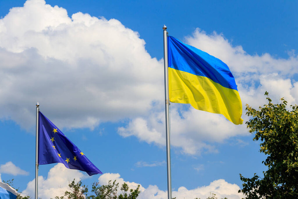 Machająca flaga Unii Europejskiej i flaga Ukrainy przeciwko błękitnemu niebu - Zdjęcie, obraz