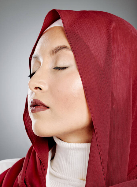 Closeup of a glowing beautiful muslim woman with eyelash extensions isolated against grey background in studio. Young woman wearing a red hijab or headscarf and jewellery. Perfect and flawless skin. - Φωτογραφία, εικόνα