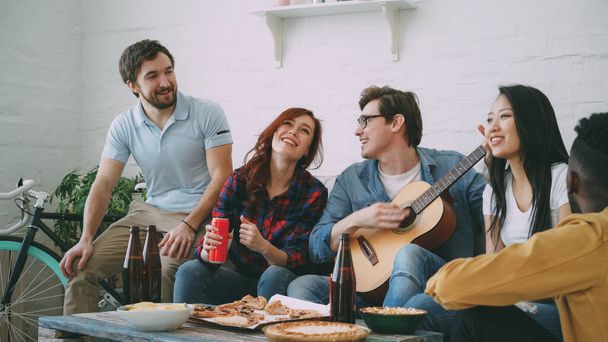 Happy mladí přátelé mají strany na sdílený byt a společné zpívání při jejich přítel doma hrát na kytaru doma - Fotografie, Obrázek