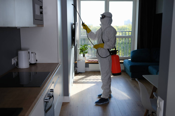 Worker in protective suit cleans room from cockroaches and rats with spray gun. Sanitary service disinfects the apartment with chemical agent - Foto, Bild
