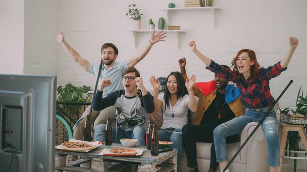 Multi ethnic group of friends sports fans with French national flags watching hockey championship on TV together cheering up their favourite team at home indoors - 写真・画像