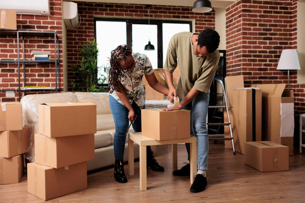 Married homeowners preparing furniture for transportation to new rented apartment flat, using sticky tape roller to pack things in boxes. Moving in family house bought on mortgage loan. - Photo, image