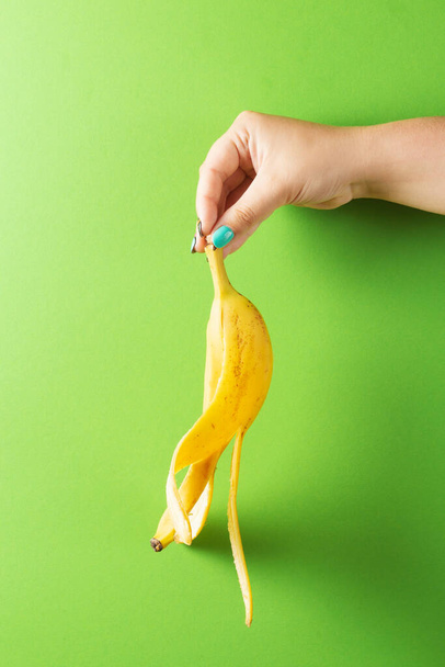 Female hand with colorful manicure holding peeled banana on green background - 写真・画像