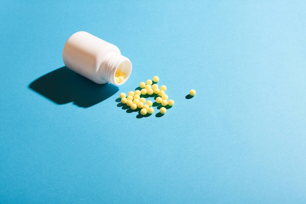 Ball pills and a white plastic bottle on blue background. - Foto, Imagem