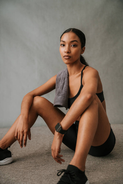 Multi Ethnic female sitting on the floor in her sportswear towel over shoulders and waiting to start work out. High quality photo - Foto, immagini