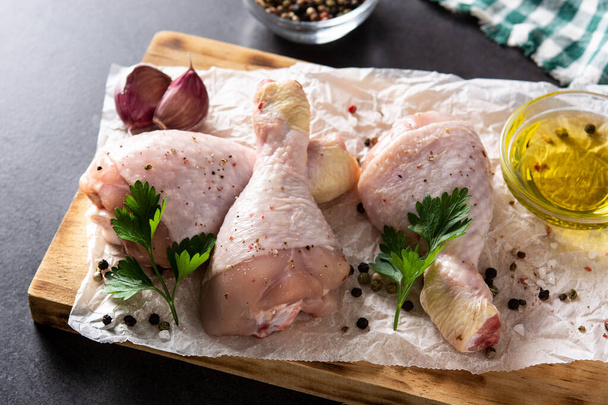Raw chicken meat legs with spices and herbs on black background - 写真・画像