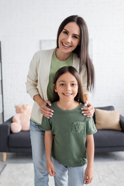 happy woman standing behind smiling child in living room  - Фото, зображення