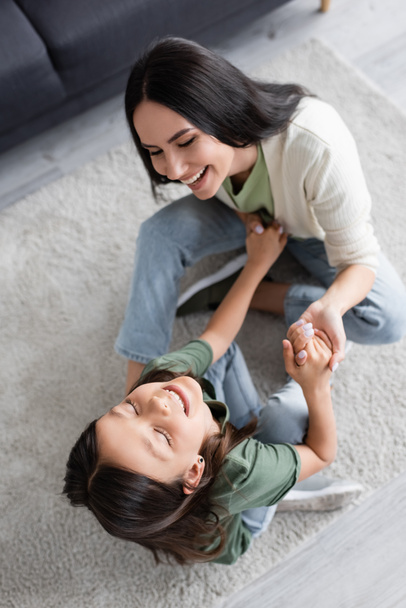 top view of cheerful babysitter and girl having fun on carpet at home - Photo, image