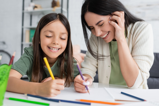 happy babysitter with closed eyes laughing while cheerful girl drawing on paper - Foto, Imagem