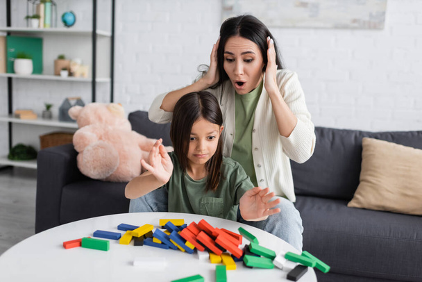 shocked nanny touching head near upset girl and colorful wooden blocks - Valokuva, kuva