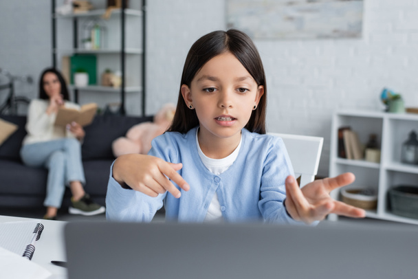 girl pointing at laptop during online lesson near nanny on blurred background - Foto, Imagen