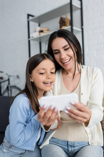 дитина і няня посміхаються біля розмитого смартфона під час відеодзвінка вдома
 - Фото, зображення