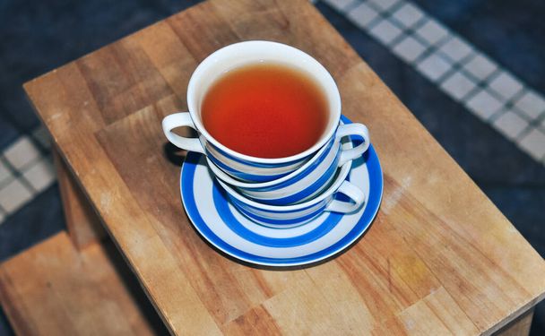 zbliżenie filiżanki czarnej herbaty z niebieskimi paskami w domu, herbata i relaks - Zdjęcie, obraz