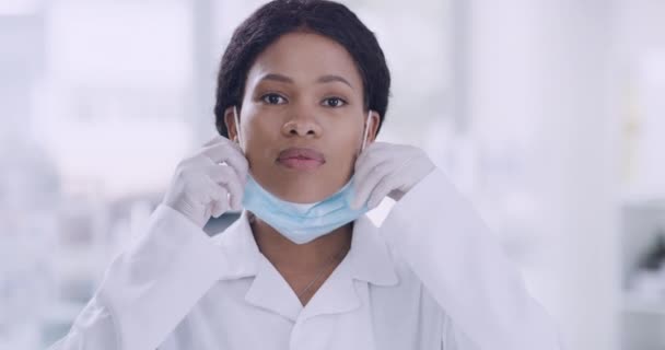 Portrait of black doctor covering her face with a mask while wearing gloves in a hospital with copyspace. Practicing precautions during the corona virus pandemic. Health and safety in the workplace. - Filmati, video