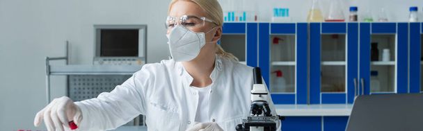 Scientist in protective mask holding test tube near microscope in laboratory, banner  - Foto, immagini