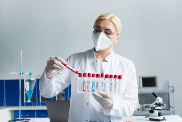 Researcher in protective mask holding test tubes with monkeypox lettering in laboratory  - Φωτογραφία, εικόνα