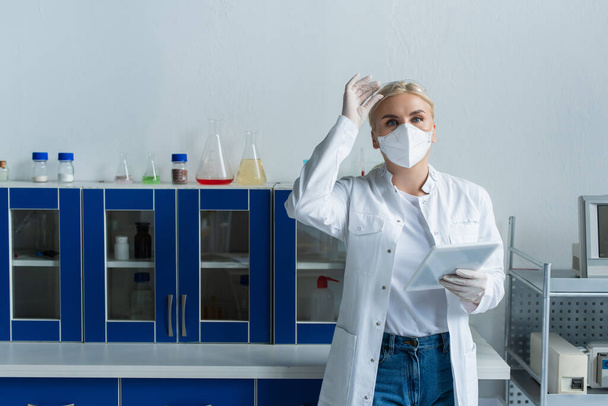 Scientist in protective mask holding goggles and digital tablet in laboratory  - Foto, imagen