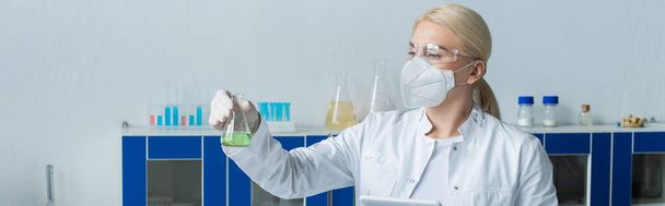 Scientist in white coat holding flask and digital tablet in lab, banner  - Foto, Imagen