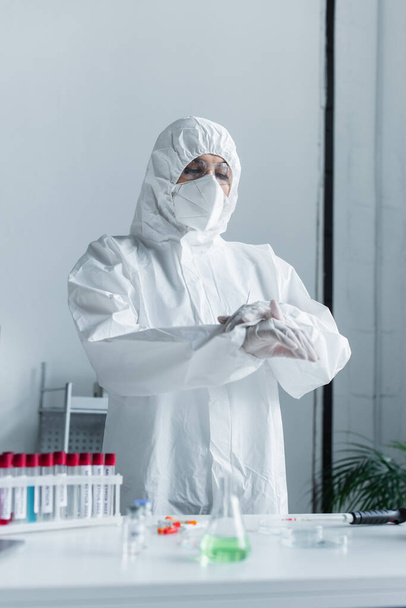 Scientist in protective suit and mask standing near blurred test tubes in lab  - Foto, Bild