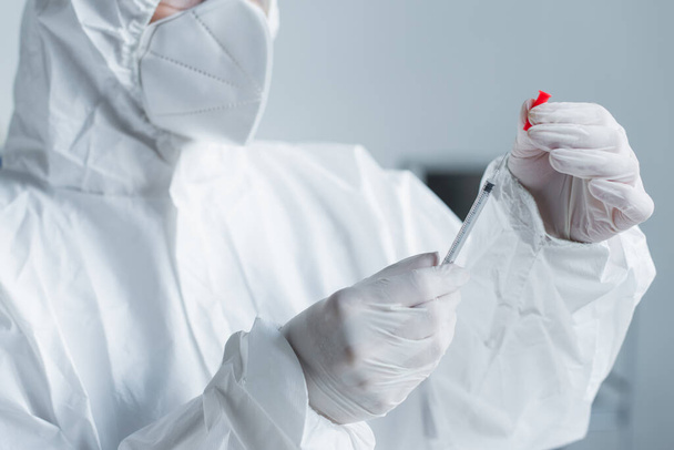 Cropped view of scientist in hazmat suit in latex gloves holding syringe in lab  - Foto, immagini