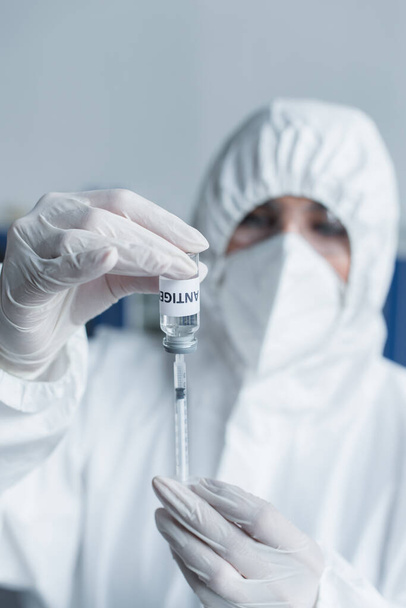 Blurred scientist in latex gloves holding antigen and syringe in laboratory - Foto, Bild